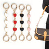 Five gold-toned heart pendant chains with black and pink beads and jump rings displayed against a white background.