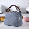 A navy blue and white striped thermal lunch bag with brown handles resting on a white surface.