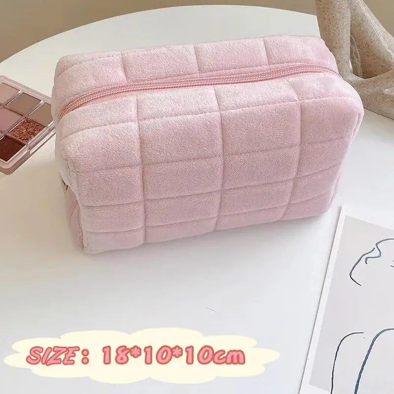 A pink quilted zippered cosmetic storage pouch lying on a white surface.