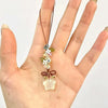 Une main tient un collier pendentif de fleur étoile transparente et givrée avec de petits accents floraux.