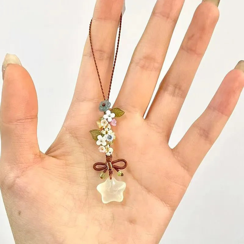 Une main tient un collier pendentif de fleur étoile transparente et givrée avec de petits accents floraux.