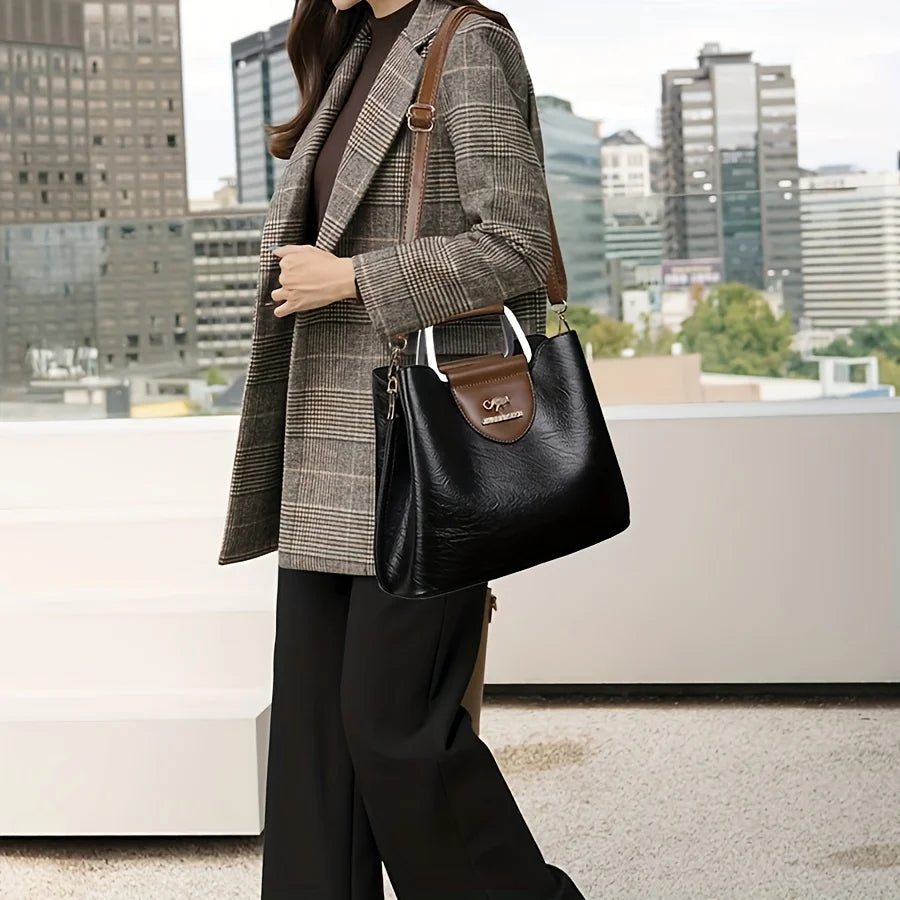 Une femme portant un blazer en tweed et un pantalon noir tient un sac bandoulière noir en cuir à multiples poches.