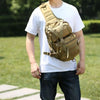 A person wearing a white t-shirt is holding a tan sling backpack.