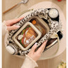 A hand is holding a floral corduroy insulated lunch box and bag filled with food on a wooden table.