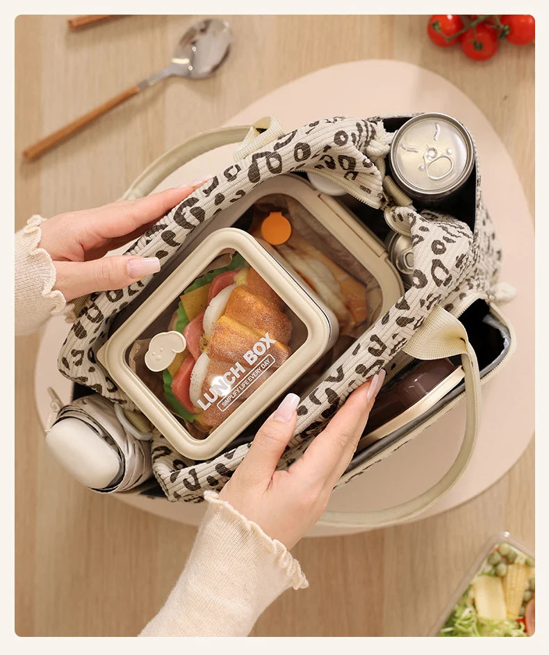 A hand is holding a floral corduroy insulated lunch box and bag filled with food on a wooden table.