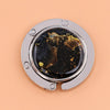 A silver folding table bag hook with a round glass lens showing a dark starry sky view.