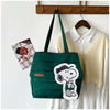 A dark green canvas tote bag featuring a white Snoopy design, hanging on a wooden rack.