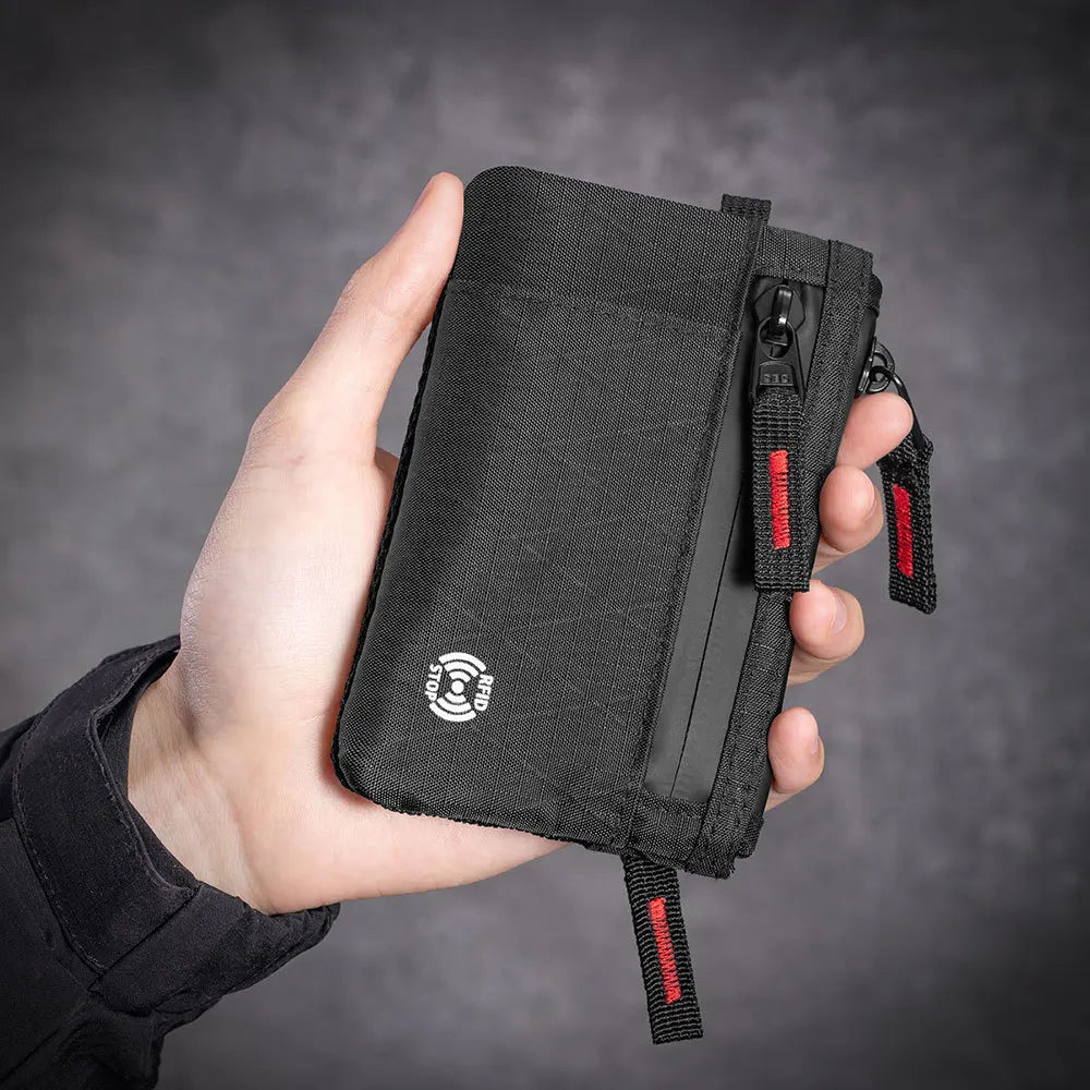 A hand holds a black RFID blocking travel wallet with an attached carabiner.