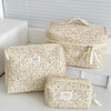A set of three floral print quilted cosmetic bags in cream and beige tones displayed on a white shelf.