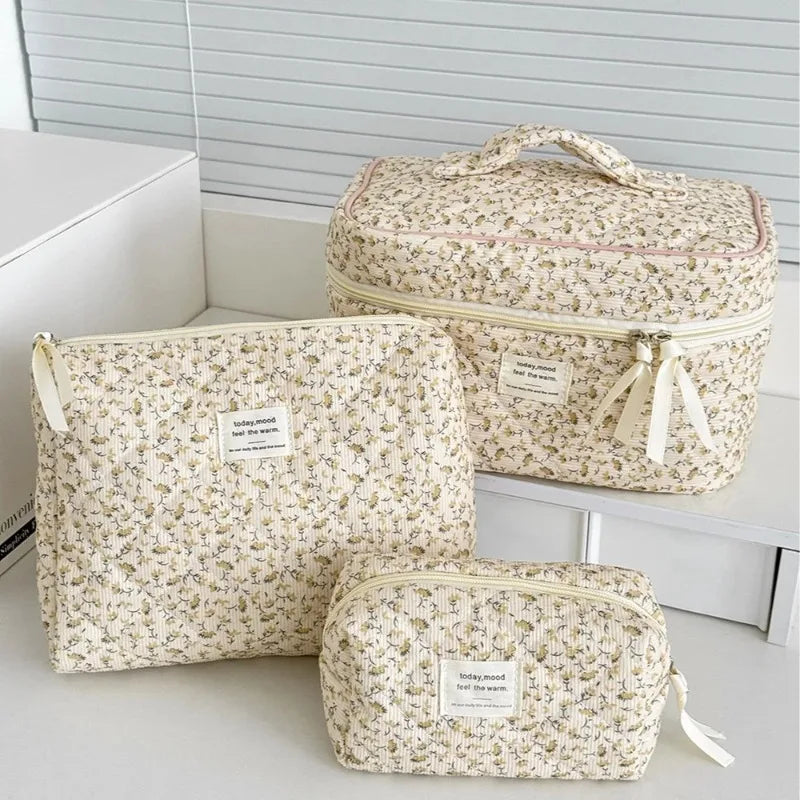 A set of three floral print quilted cosmetic bags in cream and beige tones displayed on a white shelf.