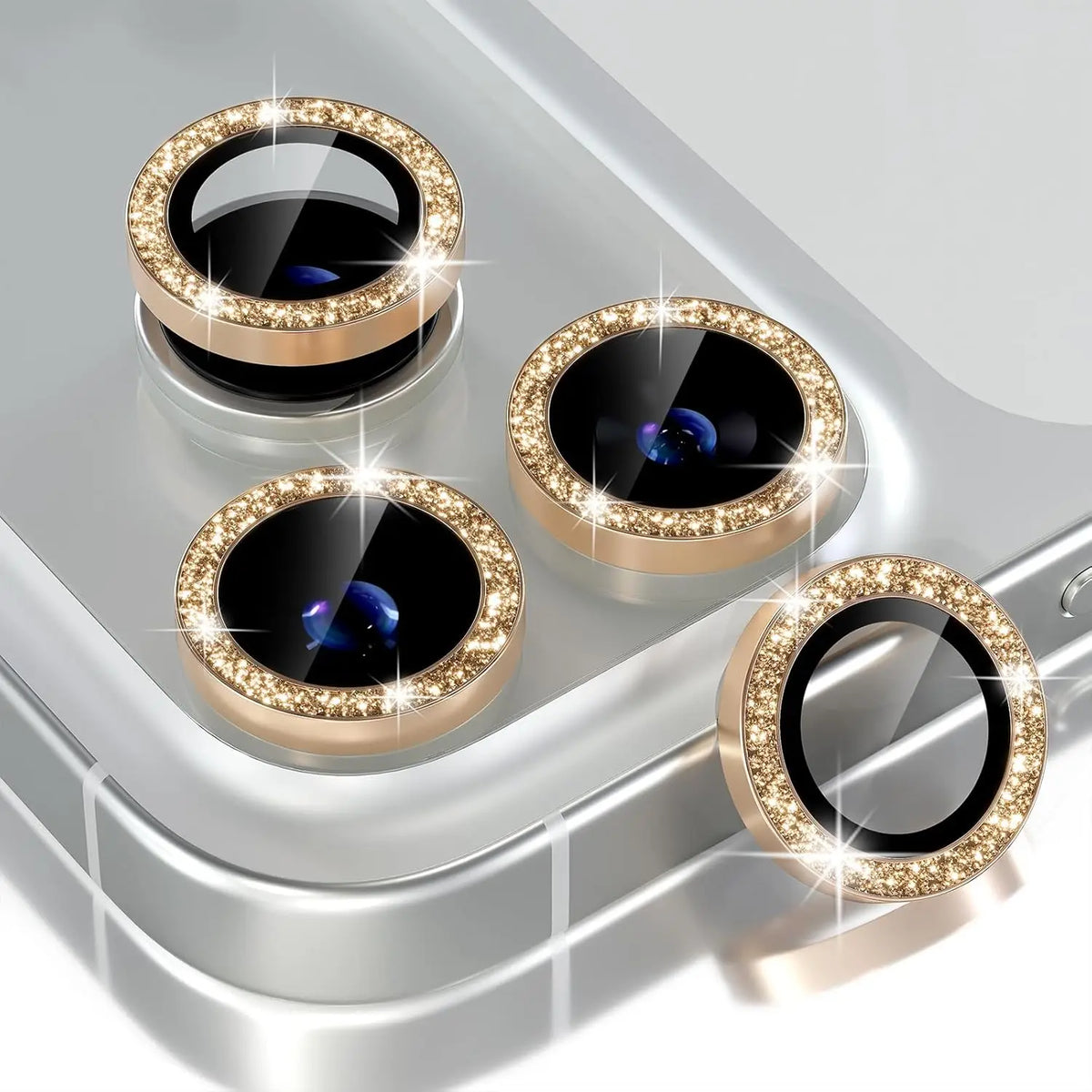 Four glitter diamond camera lens protectors with metal frames displayed on a silver surface.