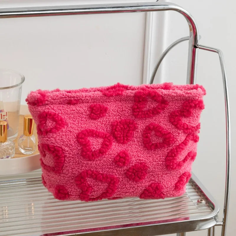 A bright pink plush storage bag with a heart pattern resting on a silver metal shelf.