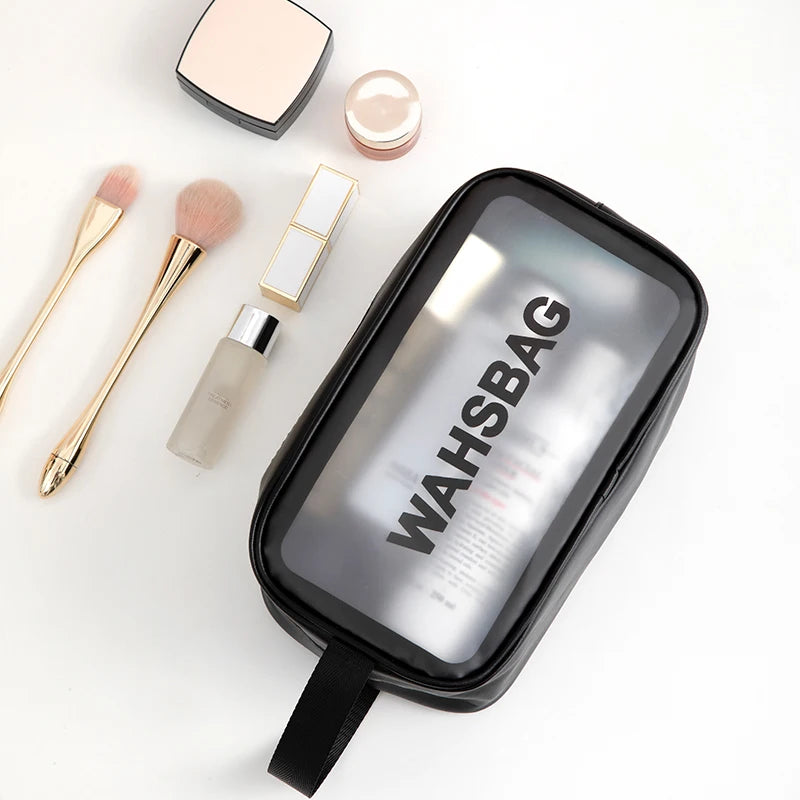 A clear waterproof travel toiletry bag with a black lid and a black strap, next to makeup brushes and powder.