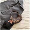 A leopard print PU leather mini tote handbag is held against a gray blazer.