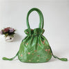 Clutch de noche con lazo brillante verde y bordado floral sobre una superficie blanca.