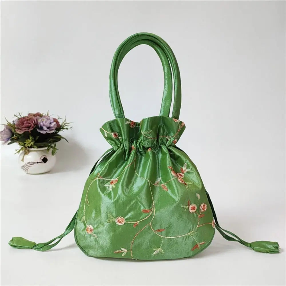 Clutch de noche con lazo brillante verde y bordado floral sobre una superficie blanca.