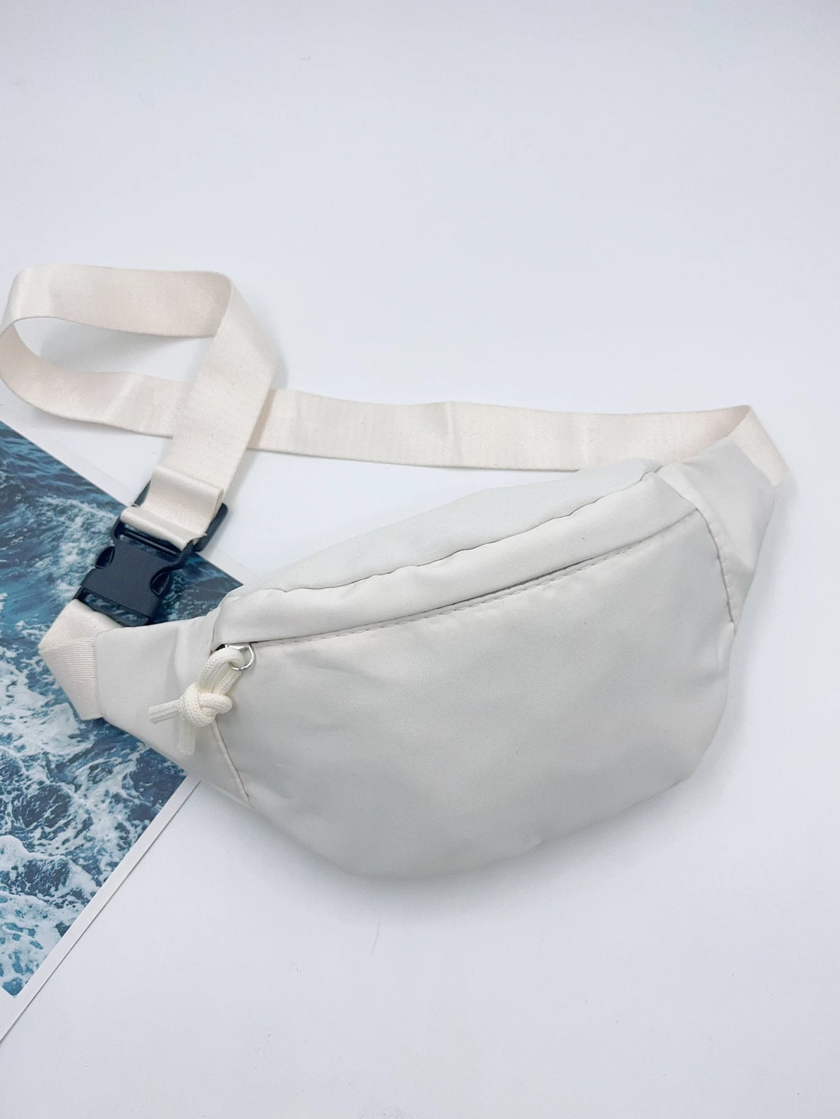 Sac bandoulière en nylon blanc avec une sangle beige clair sur fond blanc.