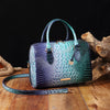 A dark purple and green crocodile pattern luxury leather crossbody tote bag resting on a wooden surface.