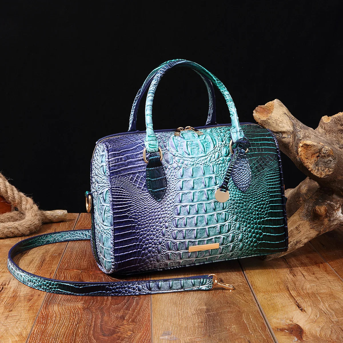 A dark purple and green crocodile pattern luxury leather crossbody tote bag resting on a wooden surface.