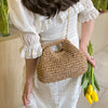 Une femme portant une robe blanche tient un sac à main en paille tissée.
