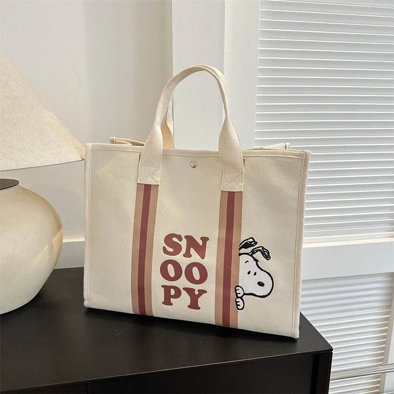 A beige canvas shoulder bag featuring a Snoopy cartoon design with brown stripes, resting on a dark surface.