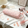 A pink quilted storage bag is displayed on a white surface next to a pink hair dryer and some rose petals.