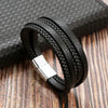 A black leather bracelet with braided texture and a silver clasp resting on a wooden surface.