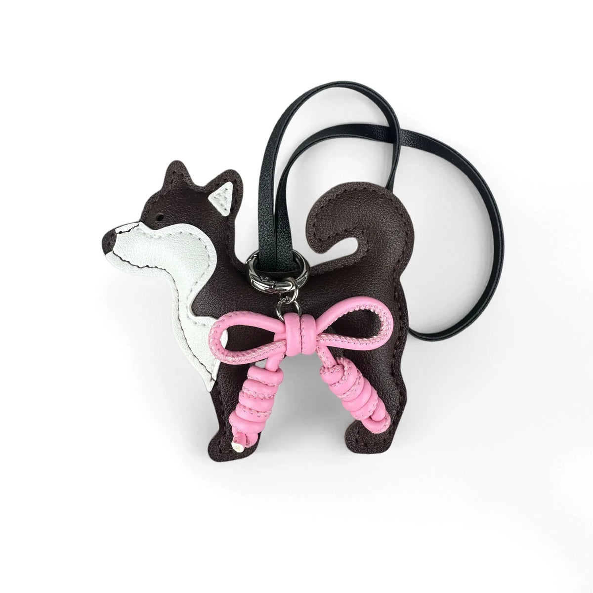 Colgante de perro Shiba Inu marrón oscuro y blanco con un lazo de cuero trenzado rosa en una correa negra.