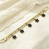 Gold chain necklace with black flower charms draped on a white lace fabric.