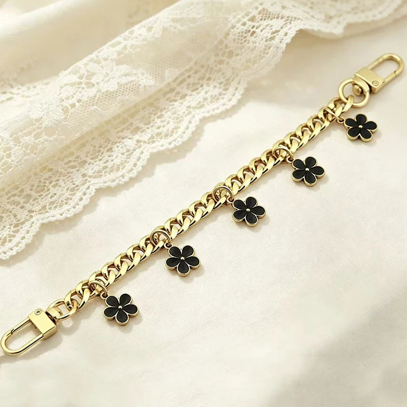 Gold chain necklace with black flower charms draped on a white lace fabric.