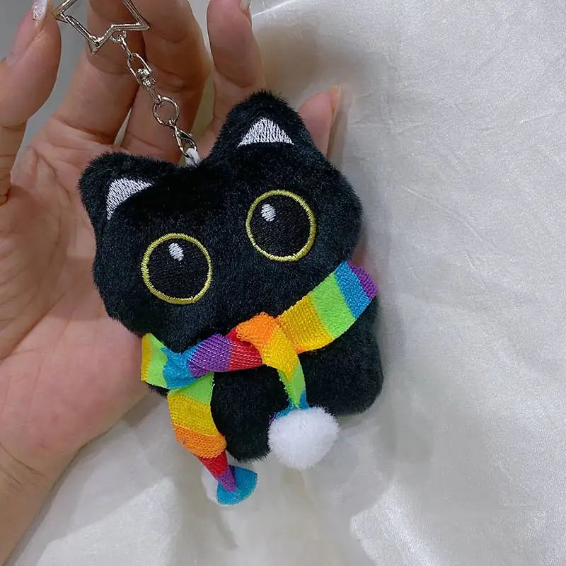 Colgante llavero de peluche de gato negro con tela de colores arcoíris, sostenido en una mano.