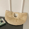 A beige rattan half-moon beach handbag displayed against a white wall.