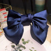 A dark blue silk bow hair clip tied in a bow shape, displayed on a white surface.