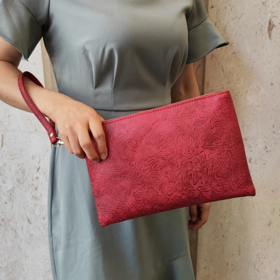 Una mujer sostiene un bolso de cuero PU con estampado floral rosa contra un vestido gris.