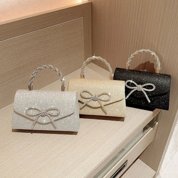 Trois pochettes de soirée en nœud pailleté argent, beige et noir présentées sur une surface claire.