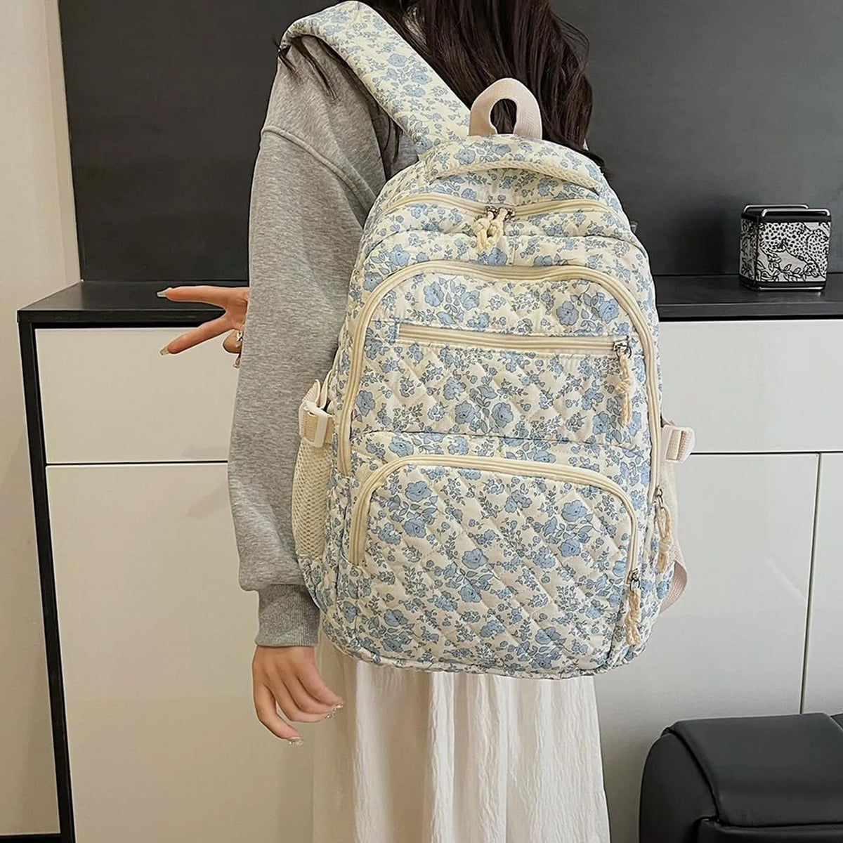 A light blue floral quilted backpack set worn by a person against a white cabinet.