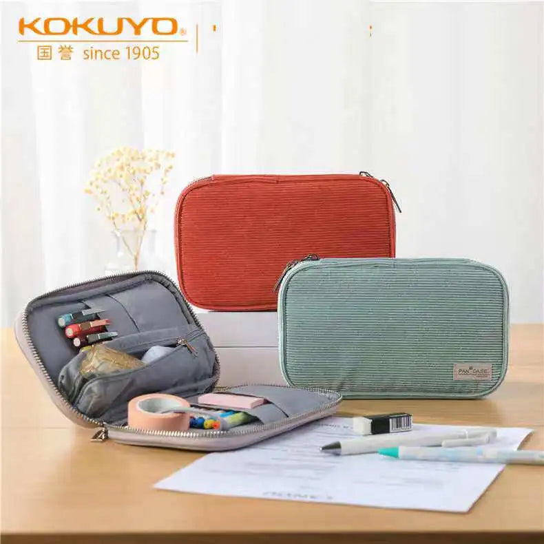 Three corduroy pencil cases in orange, green, and gray displayed on a wooden table.
