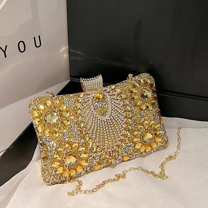 A gold rhinestone evening clutch bag with a decorative clasp resting on a white surface.