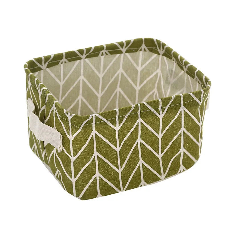 A square, olive green storage basket made of folded cotton linen with a white chevron pattern.