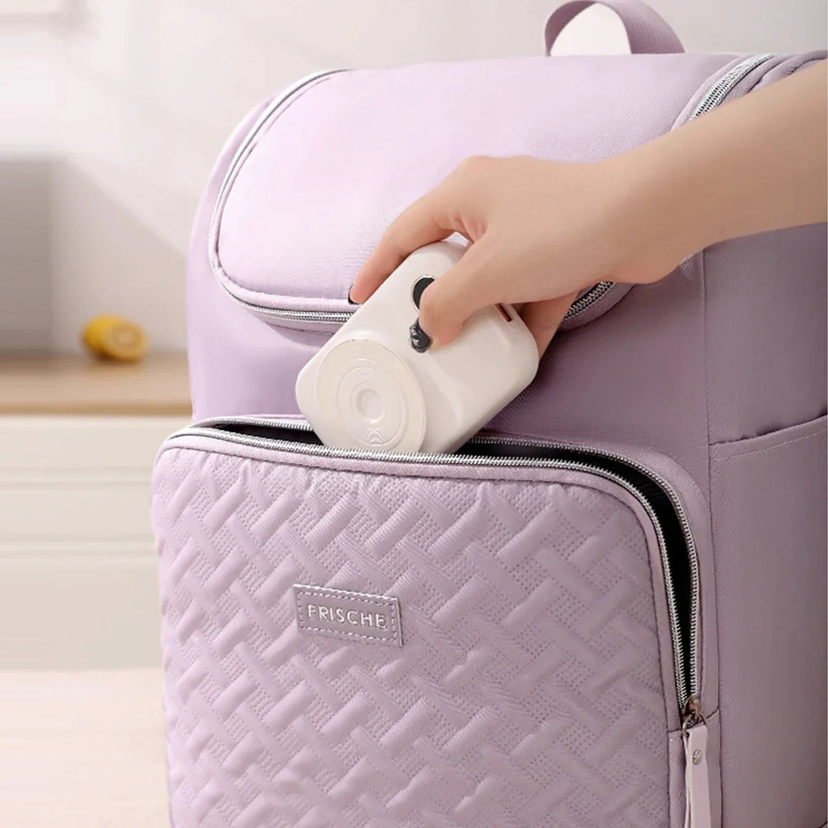 A hand is opening a purple insulated travel backpack featuring a quilted texture and a zipper.