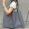 A woman holds a black and white striped foldable oxford grocery tote bag against a gray background.