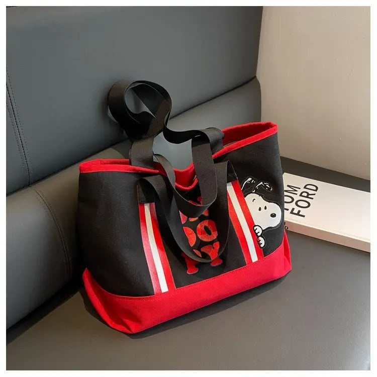 A black canvas shoulder bag featuring a Snoopy cartoon design with red and white stripes, resting on a gray surface.