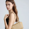 A model holds a tan leather mini shoulder bag with adjustable straps against a light gray background.