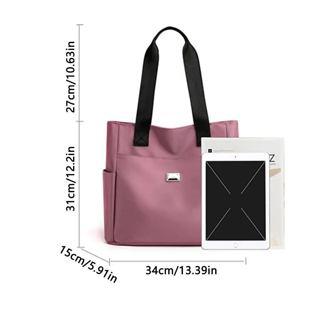 A pink nylon shoulder tote bag with black straps shown next to a white tablet.