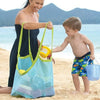 A woman and a boy are standing on a beach with a mesh storage bag and a blue bucket.