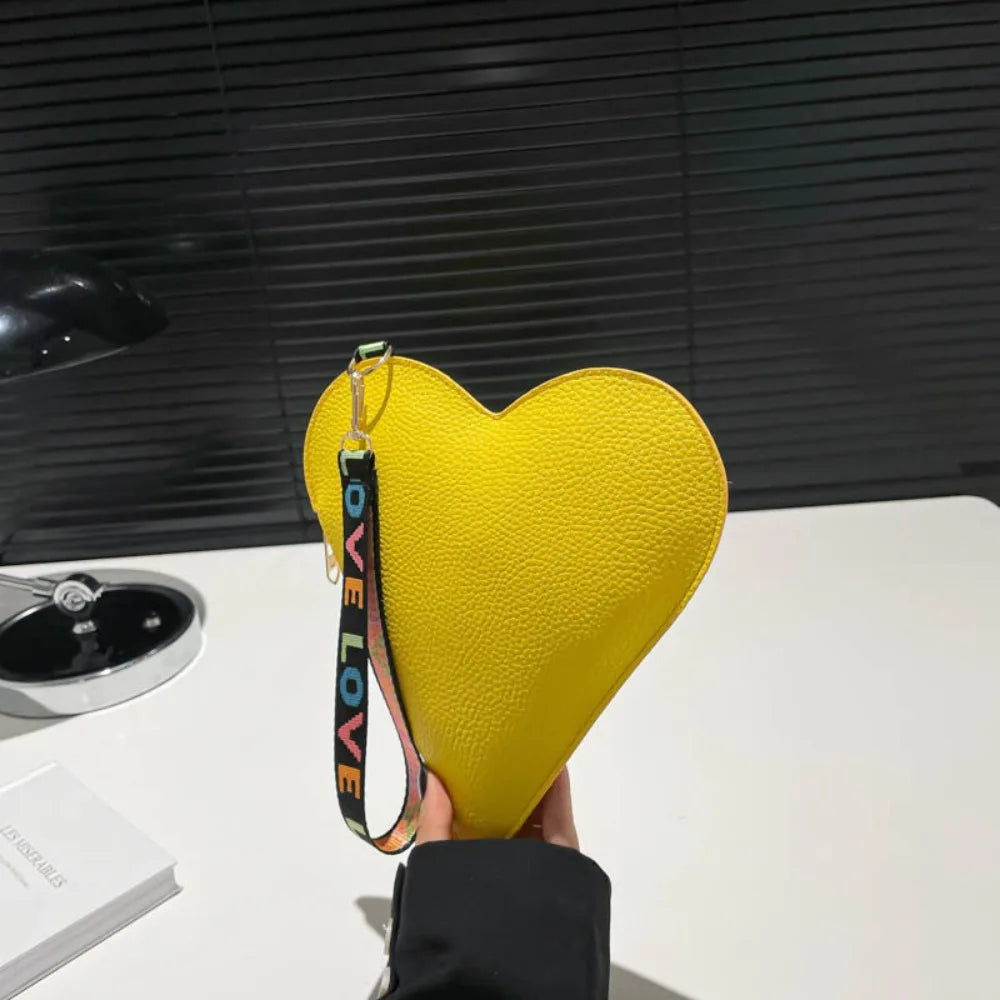 Cartera de monedas con forma de corazón de PU amarillo brillante exhibida contra un fondo oscuro.