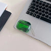 A green luminous sand effect earphone case with a silver chain resting on a laptop keyboard.