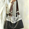 A black and white polka dot shoulder bag with a white lace overlay and brown leather straps being held by a person in a beige