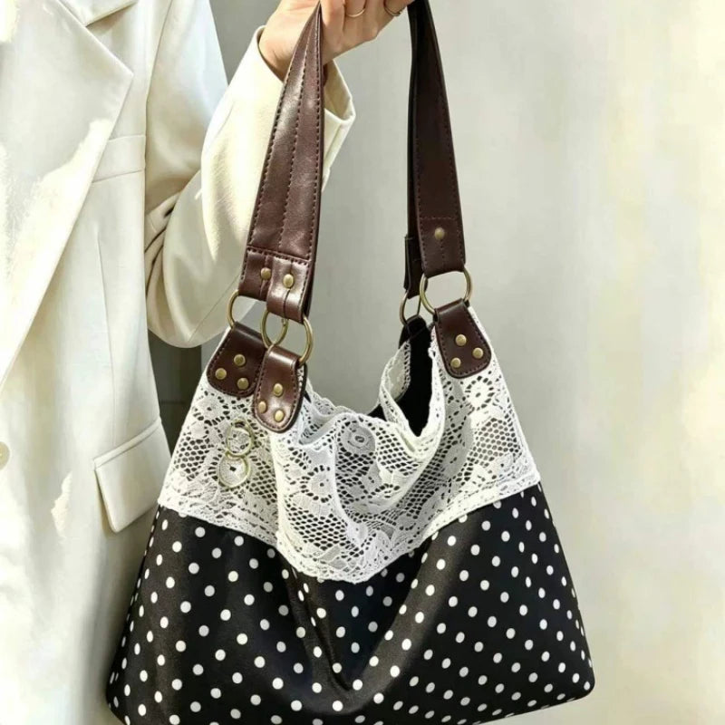 A black and white polka dot shoulder bag with a white lace overlay and brown leather straps being held by a person in a beige