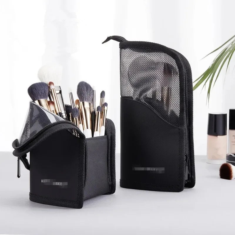 A black foldable makeup brush storage case with a mesh pocket is shown next to a white object.